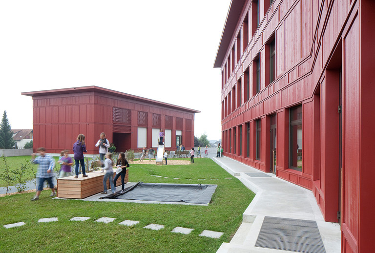 Schulhaus in Ballwil mit Holzfassade aus Fichte und roter Mittelschichtlasur